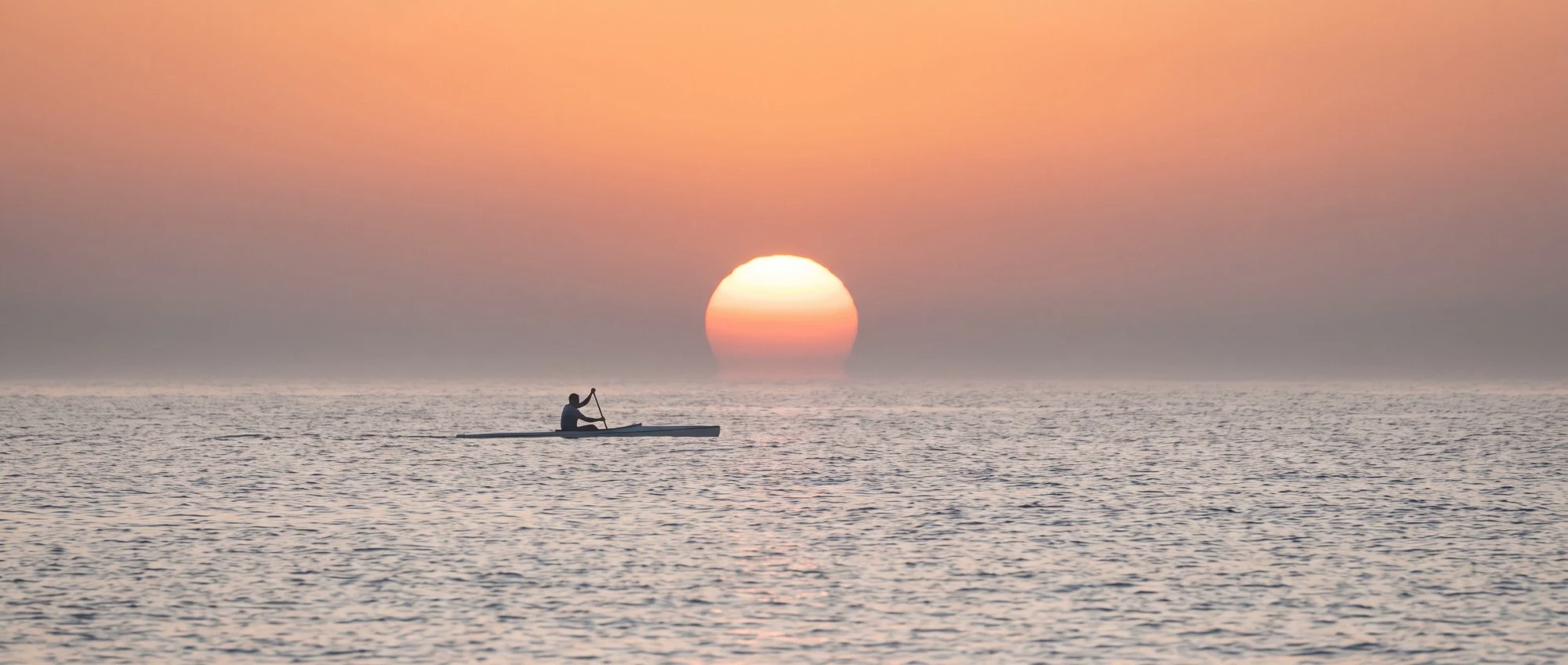 A person paddling a canoe toward the sunrise over the sea